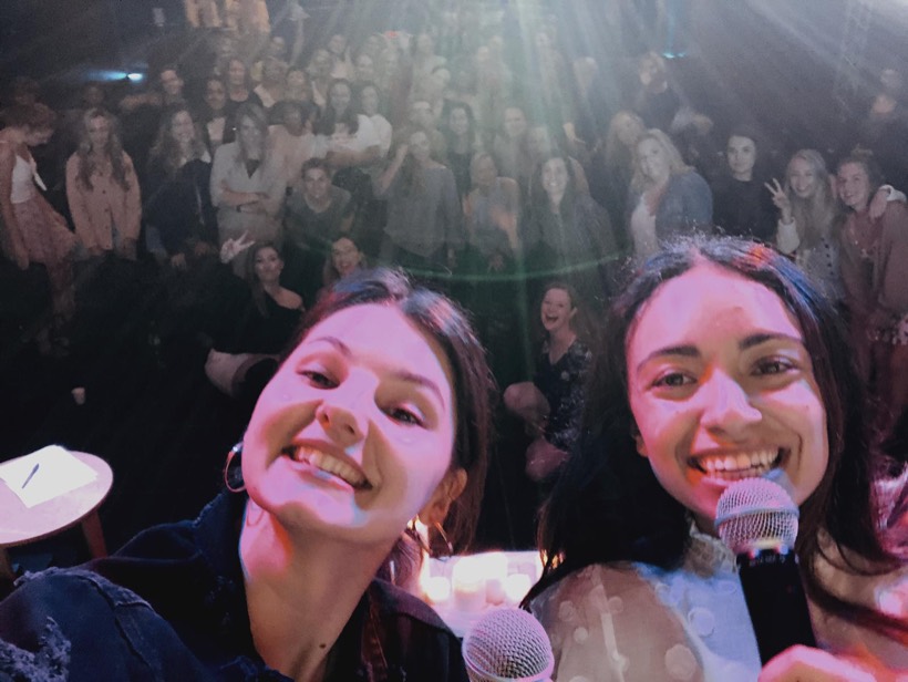 A joyful selfie with microphones and a crowd in the background.