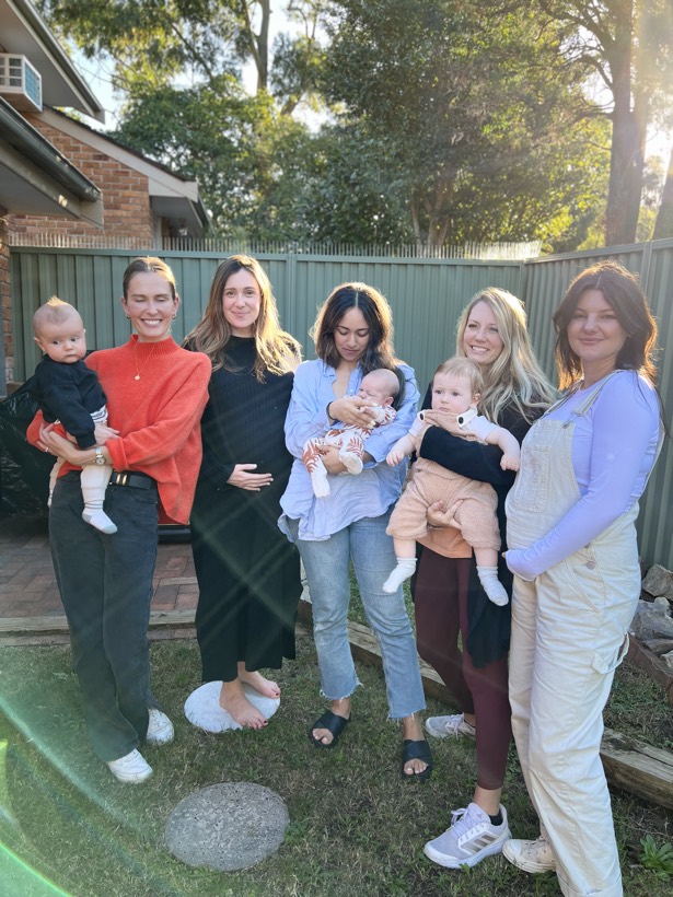 Women standing together in a sunny yard holding babies.