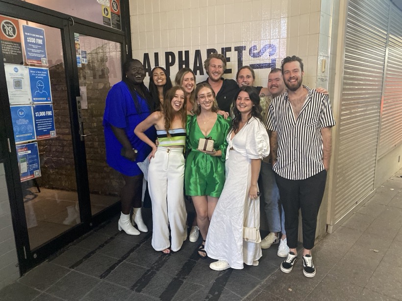 A group of friends smiling together outside at night.